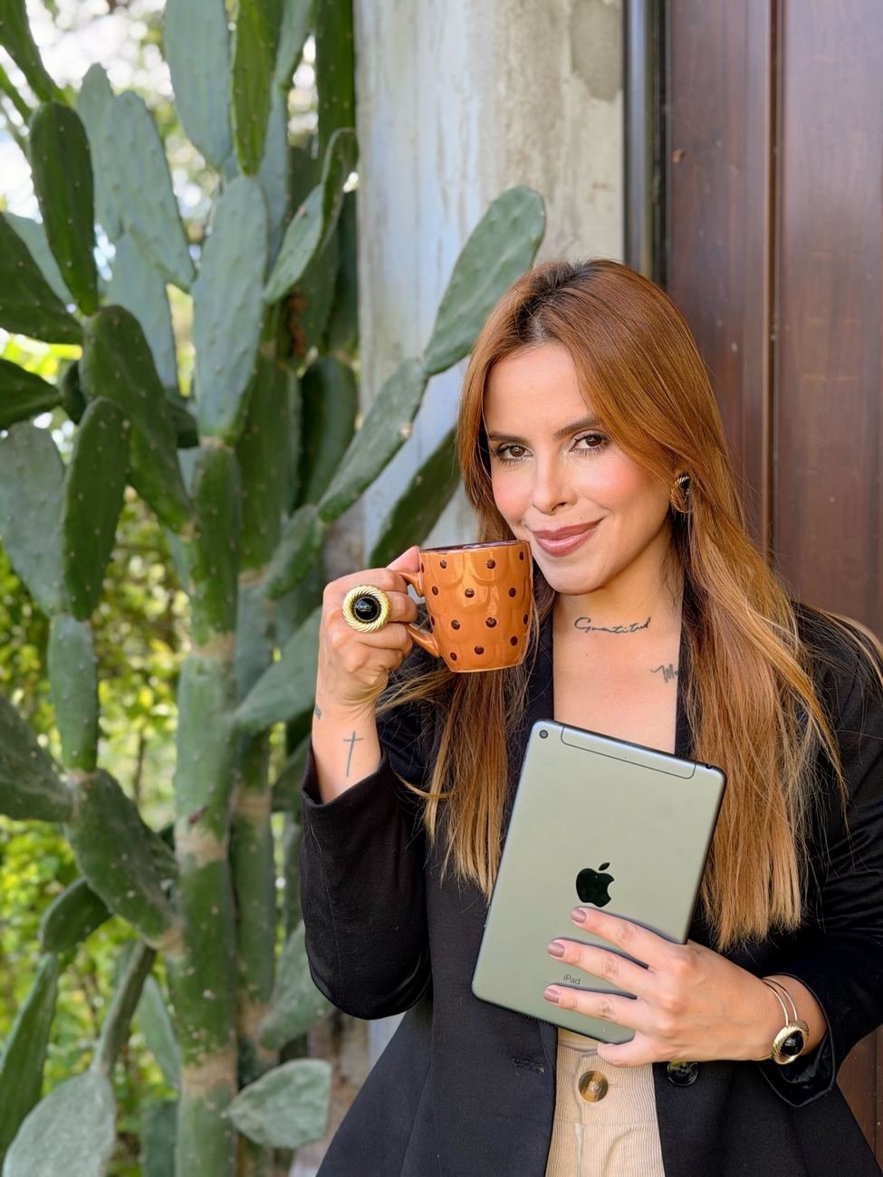 Jenn Reinoza con una taza de café y un iPad junto a un cactus